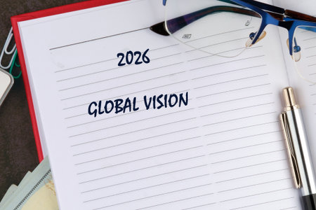 A notebook is open to a page with the year 2026 and the words GLOBAL VISION written on it. A silver pen and blue glasses sit on top of the page.の写真素材