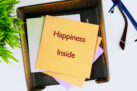 A desk organizer holds colorful sticky notes, the top one displaying Happiness Inside, alongside a small plant and glasses, suggesting a focus on positivity and mental wellbeing.の写真素材