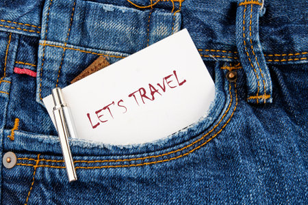 A white note card with the phrase LETS TRAVEL is sticking out of a blue jeans pocket, accompanied by a pen, hinting at trip planning and excitement.の写真素材