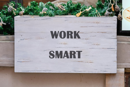 A simple message encourages wise decision-making. The sign says WORK SMART in dark letters and sits beneath green garlands decorated with pine cones and holiday ornaments.の写真素材