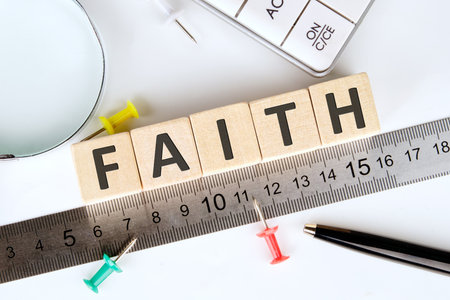 The word FAITH is spelled out using wooden blocks, resting beside a ruler, pins, calculator, pen, and a magnifying glass. The scene encourages reflection on beliefs and measurement.の写真素材