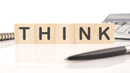 Wooden blocks spelling THINK sit on a white surface with a notepad, pen and calculator. The arrangement inspires creative brainstorming and problem-solving.の写真素材