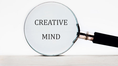Close-up of the phrase CREATIVE MIND as seen through a magnifying glass, symbolizing focus on ingenuity, problem-solving, and visionary thinking on a light surface.の写真素材