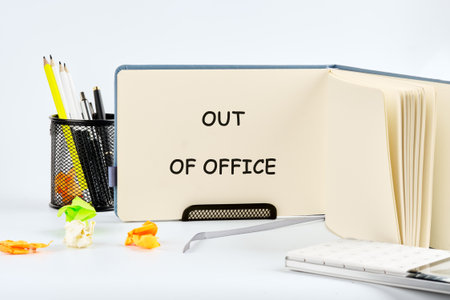 A sign displays Out of Office. A full pen holder sits next to it. Crumpled papers are scattered on the desk. It suggests the individual has left for a vacation or day off.の写真素材