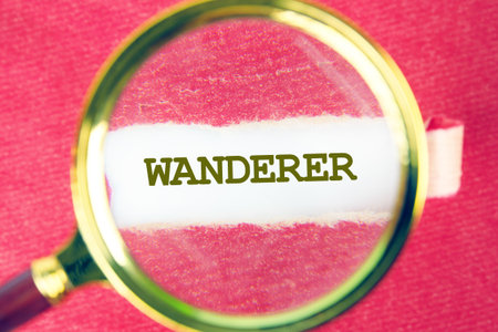 A close-up view centers on a magnifying glass highlighting the word Wanderer, set against a textured crimson backdrop, evoking a sense of adventure and discovery.の写真素材