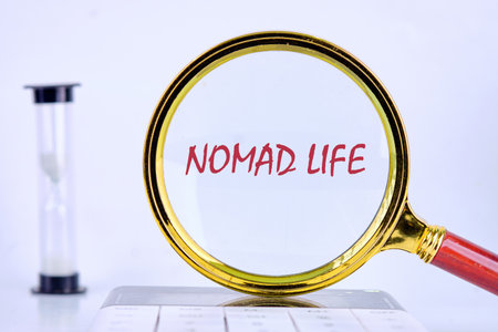 The words NOMAD LIFE are magnified by a gold magnifying glass, while an hourglass sits to the side. A white keyboard partially appears at the bottom.の写真素材