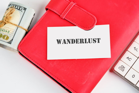 A stack of money, a red notebook with a Wanderlust card, and a calculator suggest planning for upcoming travel adventures and managing travel budgets.の写真素材