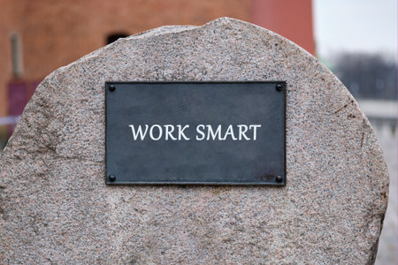 A plaque that reads WORK SMART is mounted on a large, rough stone in what appears to be a park. The sky is overcast, suggesting a cool, possibly autumn day.の写真素材