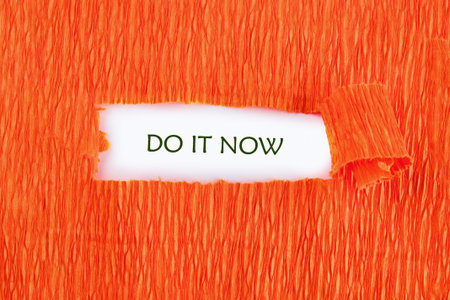 Orange crepe paper is torn to reveal Do It Now written in green on a white background, creating an immediate and urgent call to action.の写真素材