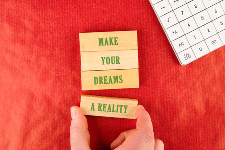 Hands arrange wooden blocks that showcase an inspirational message about making dreams a reality....