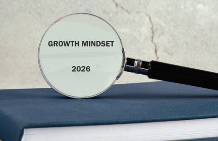 A magnifying glass highlights the words growth mindset and the year 2026, resting on a blue book,...