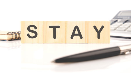 Wooden letters spell out the word stay, placed on a bright surface alongside a pen and calculator. This setup encourages a positive mindset for productivity in any office.の写真素材