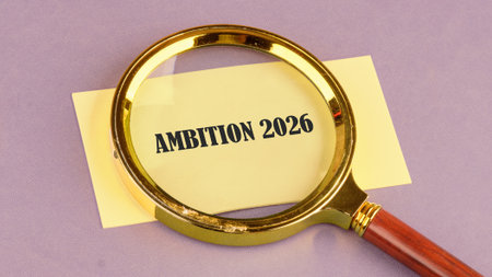 A golden magnifying glass rests on a yellow paper displaying the words ambition 2026, symbolizing a clear focus on future plans and dreams with determination and purpose.の写真素材