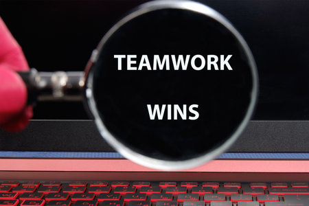 A hand holds a magnifying glass over bold text that reads teamwork wins, symbolizing the power and...