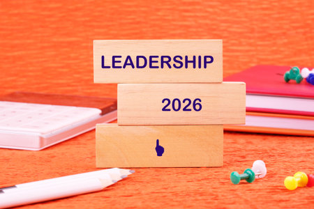 A bright orange surface showcases wooden blocks stacked with the words Leadership and 2026. Colorful stationery items like notebooks and pins surround this inspiring setup.の写真素材