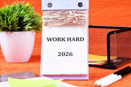 A calendar rests on a vibrant orange surface, featuring the phrase WORK HARD prominently displayed.