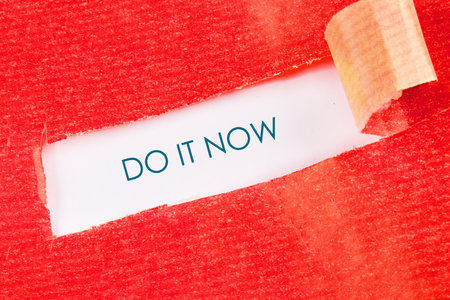 A call to action is revealed, showcasing the phrase Do it now on a white background peeking through a torn red material. The scene evokes a feeling of pressing urgency.の写真素材