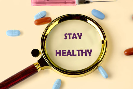 On a plain background, medicine in pill form and a pink syringe are scattered around a glaming...