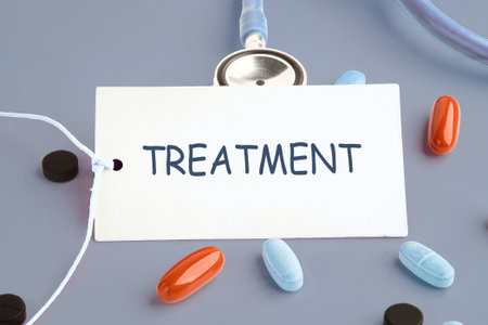 On a gray surface, a card labeled treatment is displayed with a stethoscope draped above and pills of varying colors scattered around the card.の写真素材