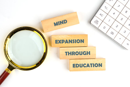 A magnifying glass rests near wooden blocks spelling out MIND EXPANSION THROUGH EDUCATION along with...