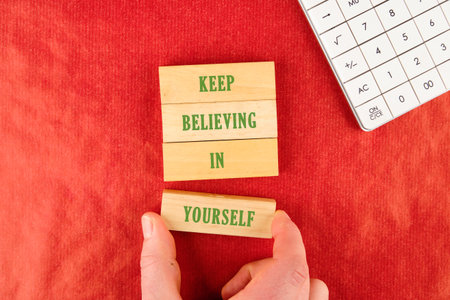 Hand positions a wooden block that reads YOURSELF to finish the phrase KEEP BELIEVING IN beside a...
