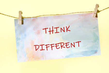 A colorful paper with the words Think Different written in red ink hangs by clothespins on a string....