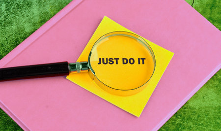 A magnifying glass focuses on the motivational phrase Just Do It, written on a yellow sticky note....
