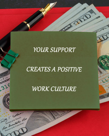 A green sticky note featuring the text YOUR SUPPORT CREATES A POSITIVE WORK CULTURE rests on several 100 US Dollar bills.の写真素材