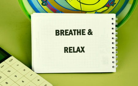 A white spiral bound notepad sits on a smooth green surface, displaying the bold words BREATHE and...