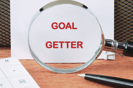 A magnifying glass magnifies the words GOAL GETTER written in red on white paper. A pen and...