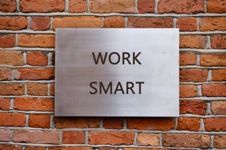 Shiny metal plaque engraved with the phrase WORK SMART, positioned on a textured red brick wall.の写真素材