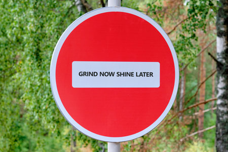 Against a backdrop of lush trees, a striking red sign boldly states the message to grind now and shine later, motivating those who see it to strive for success.の写真素材