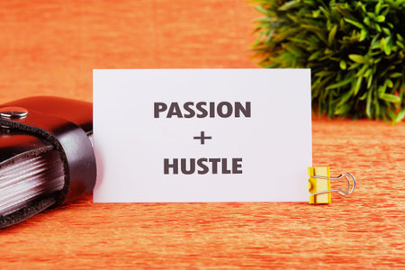 Bright orange surface showcases a motivational card highlighting passion and hustle, paired with a sleek notebook and a touch of greenery, inspiring creativity.の写真素材
