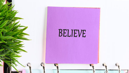 Purple BELIEVE note on white binder, green plant. Inspire positivity.の写真素材