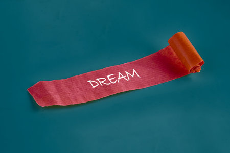 A vivid red textured strip with the white word DREAM slowly unrolls on a smooth dark teal surface,...