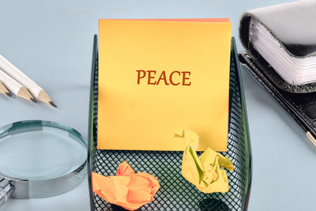 A vibrant yellow sticky note displaying the word PEACE sits firmly in a desk caddy, contrasting with two crumpled yellow papers beneath it.の写真素材
