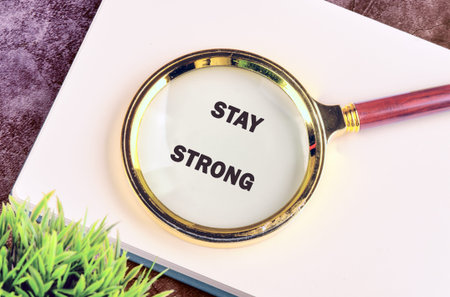 A golden magnifying glass with a wooden handle rests on a pristine white book, brilliantly illuminating the inspiring words Stay Strong.の写真素材