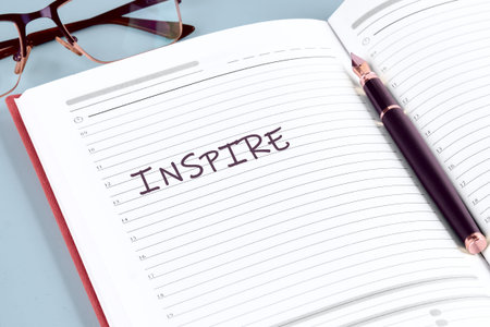 An open daily planner rests on a cool blue surface, revealing the word INSPIRE beautifully inscribedの写真素材