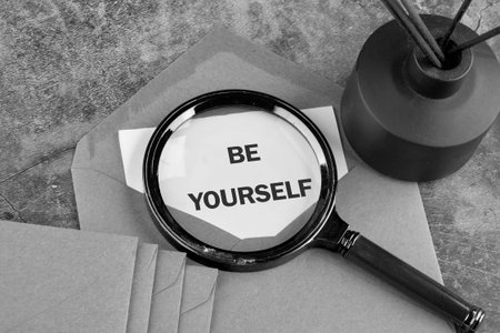 A magnifying glass highlights the phrase be yourself on a paper note.