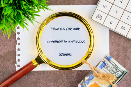 Magnifying glass on thank you for learning note, on desk with calculator, plant, and tied dollar...