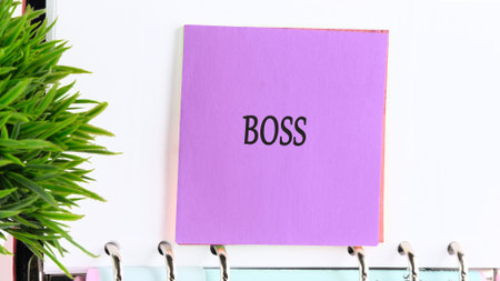 A striking purple sticky note, with Boss boldly written, is affixed to a white ring binder,...
