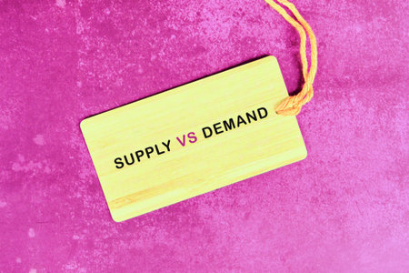 Light yellow wooden tag with SUPPLY VS DEMAND on magenta background, adorned with a yellow string