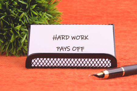 A white card presenting the motivating phrase hard work pays off rests in a holder. A sleek fountain...