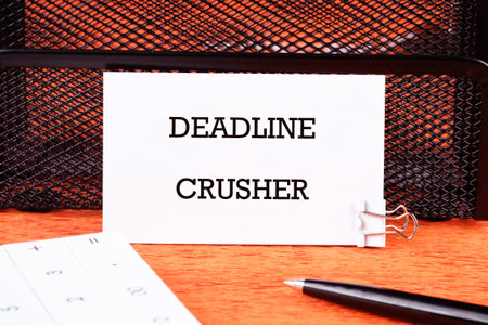 White card with DEADLINE CRUSHER text stands on a wooden desk, a calculator and pen nearby,...