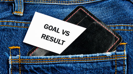 A sleek wallet is tucked into the back pocket of denim jeans, with a card showing the words goal and result. The scene captures a moment of ambition and reflection.