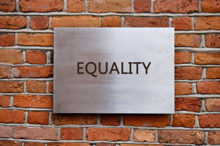 The sign with the word equality is placed on a metal plate attached to a brick wall. The setting appears to be in a city location during daylight.