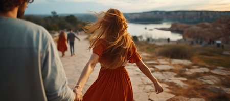 Back view of young couple in love holding hands and walking on the beachの素材