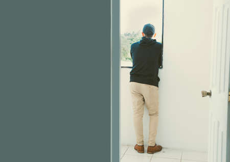 Boy from back to window, young man from back looking out window