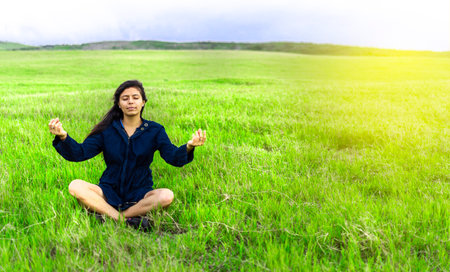 Woman in the field sitting meditating, woman doing yoga in the cool fieldの写真素材