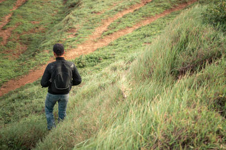 Backpacker man walking in the countryside, adventurous man descending from a hill, man with backpack going down a hillの写真素材